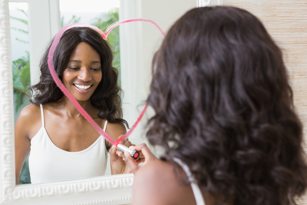 Woman drawing heart and looking at her reflection in the mirror